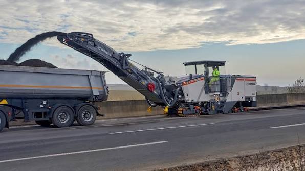 Milling machine loading reclaimed asphalt onto a truck on a highway