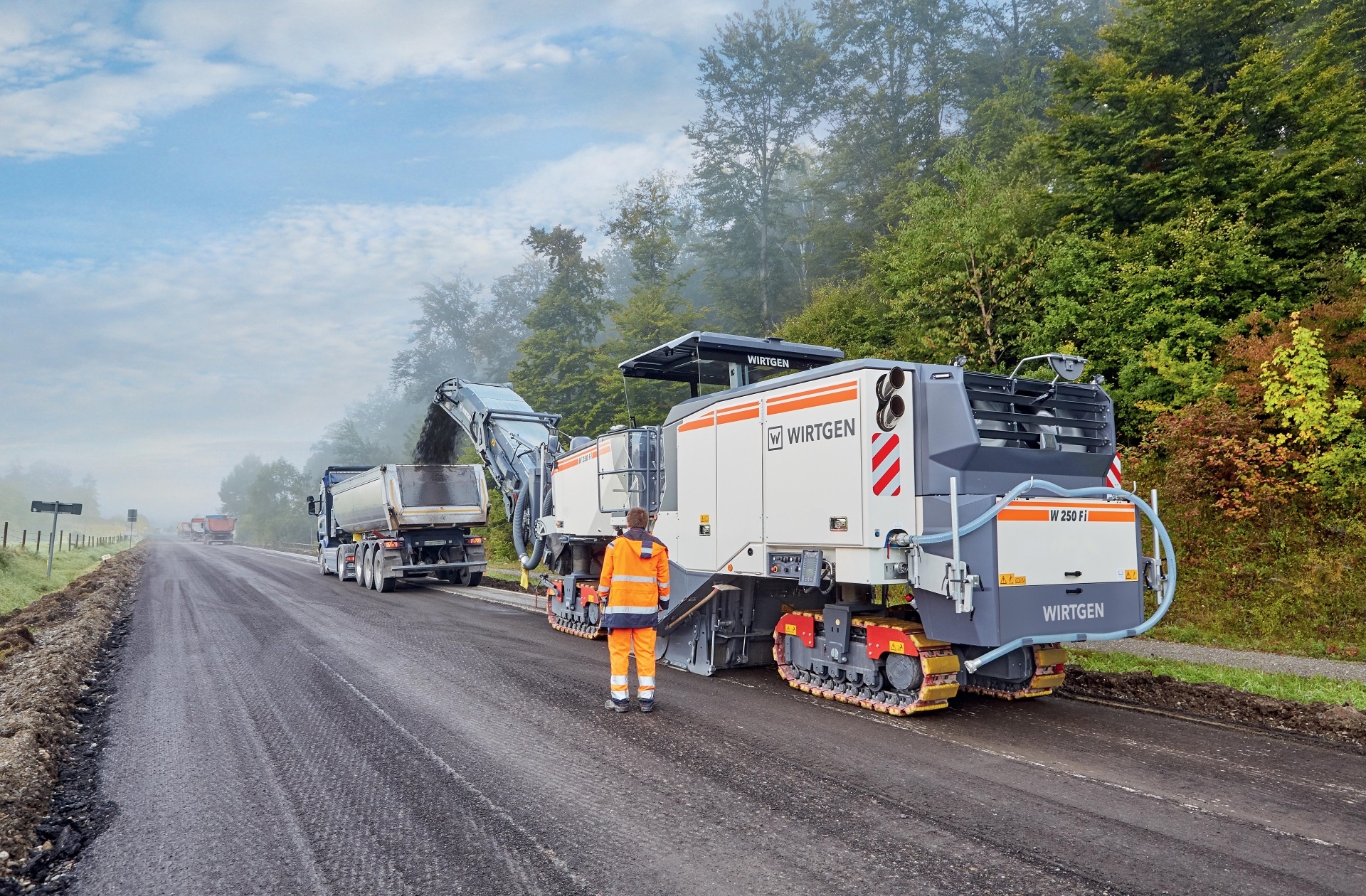 Milling machine loading material onto a truck on a misty rural road